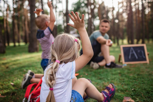 powrót do szkoły. przedszkolaki i podstawowi uczeni siedzący z nauczycielem na trawie na zajęciach plenerowych - teacher child preschool mathematics zdjęcia i obrazy z banku zdjęć