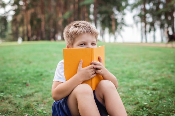 istock Back to school. Kindergarten scholar sitting on green grass with book at open-air class 1271517024