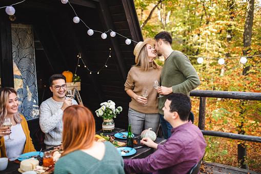 Excited young couple announcing their engagement during gathering with their friends on a autumn lunch at the log cabin patio