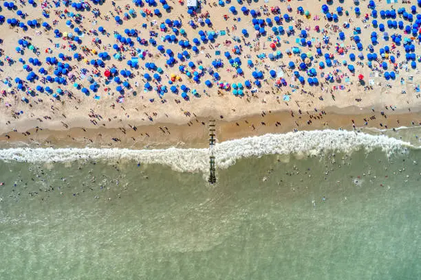Photo shows many people having summer holiday at Rehoboth Beach Delaware. There are many colorful umbrellas, people with beach activities and swimming in sea. Photo took with a drone.