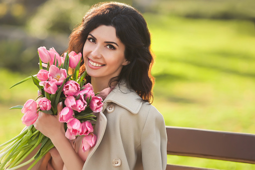 Closeup portrait of beautiful woman smiling with a braces holding bouquet of pink tulips and sitting in a park one spring day
