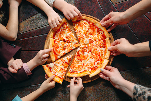 Hands taking pizza slices from wooden table, close up view
