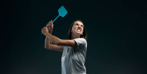 angry woman killing mosquitoes with a fly swatter - aggression control clothing image type imagens e fotografias de stock