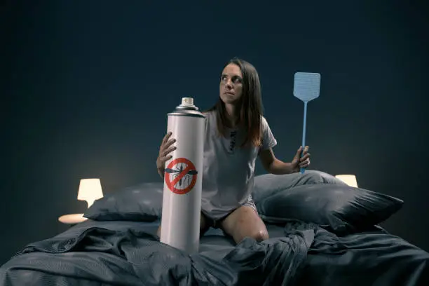 Photo of Woman killing mosquitoes with swatter and huge repellent spray