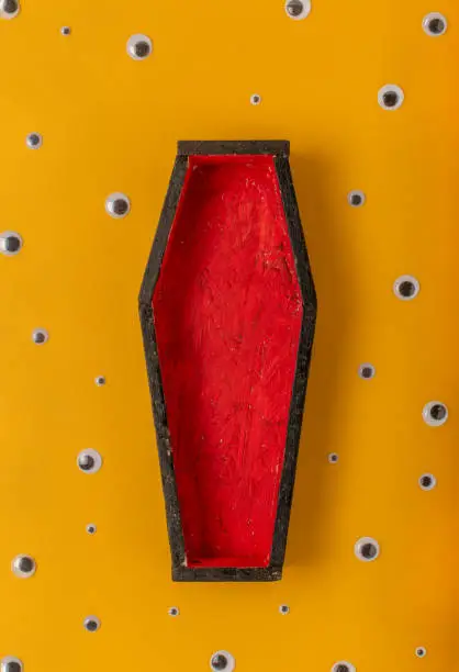 Halloween yellow background with an open red-black coffin in the center, around a scattering of plastic eyes of different sizes. A place for your product