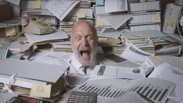 Stressed businessman buried under a lot of paperwork, he is angry and screaming