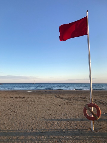 A red flag at the beach on sunny sunset of Netuno in Rome, italy