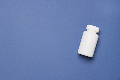 White plastic medical container for pills on right side of blue background with copy space.