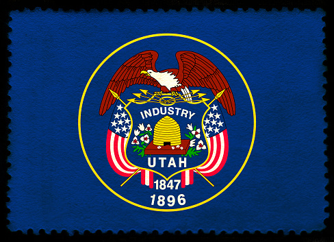 United States Utah state flag on the old grunge postage stamp isolated on black background. Texture of old paper