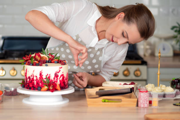 クリームとケーキの調理と装飾。赤いベルベットケーキを飾るキッチンで若い女性パティシエ - cake women confectioner photography ストックフォトと画像