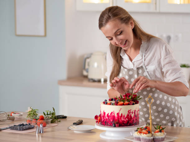 クリームとケーキの調理と装飾。赤いベルベットケーキを飾るキッチンで若い女性パティシエ - cake women confectioner photography ストックフォトと画像