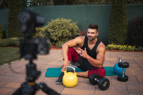 istock Male athlete sitting on exercise mat and making vlog at backyard. 1271537282