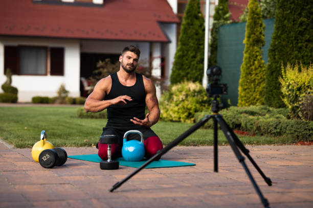 istock Male athlete sitting on exercise mat and making vlog at backyard. 1271537346