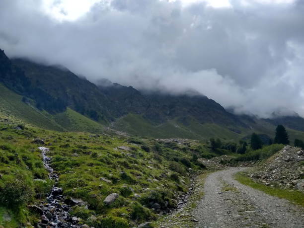 istock alpine street with little stream through clouded Austrian Alps 1271538000