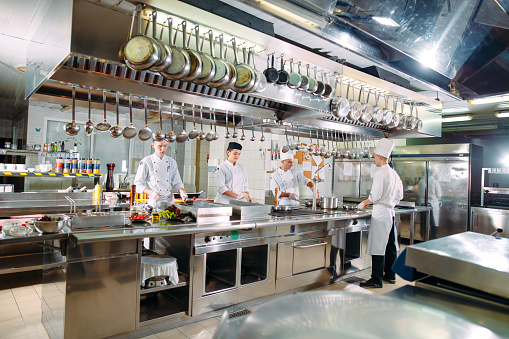 Latin American chef decorating a plate under a hot lamp while working at a commercial kitchen