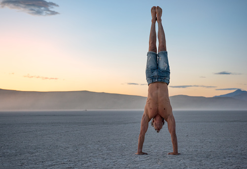Athletic handsome man pressing a handstand in the middle of a dusty desert playa. Nikon D850. Converted from RAW.