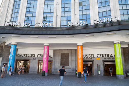 People leaving and entering station Brussels Central in summertime. Above entrance and at facade are letters Brussels Centrale. Between doors are different colored columns