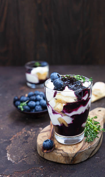 Dessert from mascarpone or ricotta cheese, blueberries and biscuit in glass on a dark background. No baked cheesecake or tiramisu. Dessert from mascarpone or ricotta cheese, blueberries and biscuit in glass on a dark concrete background. No baked cheesecake or tiramisu. yogurt fruit biscotti berry fruit stock pictures, royalty-free photos & images