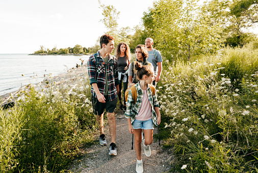 Caucasian family go walking at a lake with three children. Siblings in front of mom and dad walking and talking.