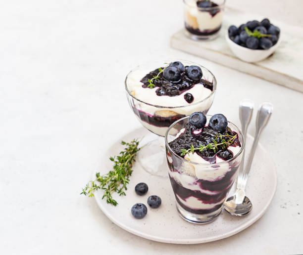 Tiramisu. Homemade dessert in glasses with blueberries, cream and ladyfingers garnish with blueberries and thyme. Light grey stone background. Tiramisu. Homemade dessert in glasses with blueberries, cream and ladyfingers garnish with blueberries and thyme. Light grey background. yogurt fruit biscotti berry fruit stock pictures, royalty-free photos & images