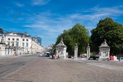 Street Rue Royale and Par of Brussels in summertime. A few people are walking in scene. At right side is entrance to public park. At left side are buildings