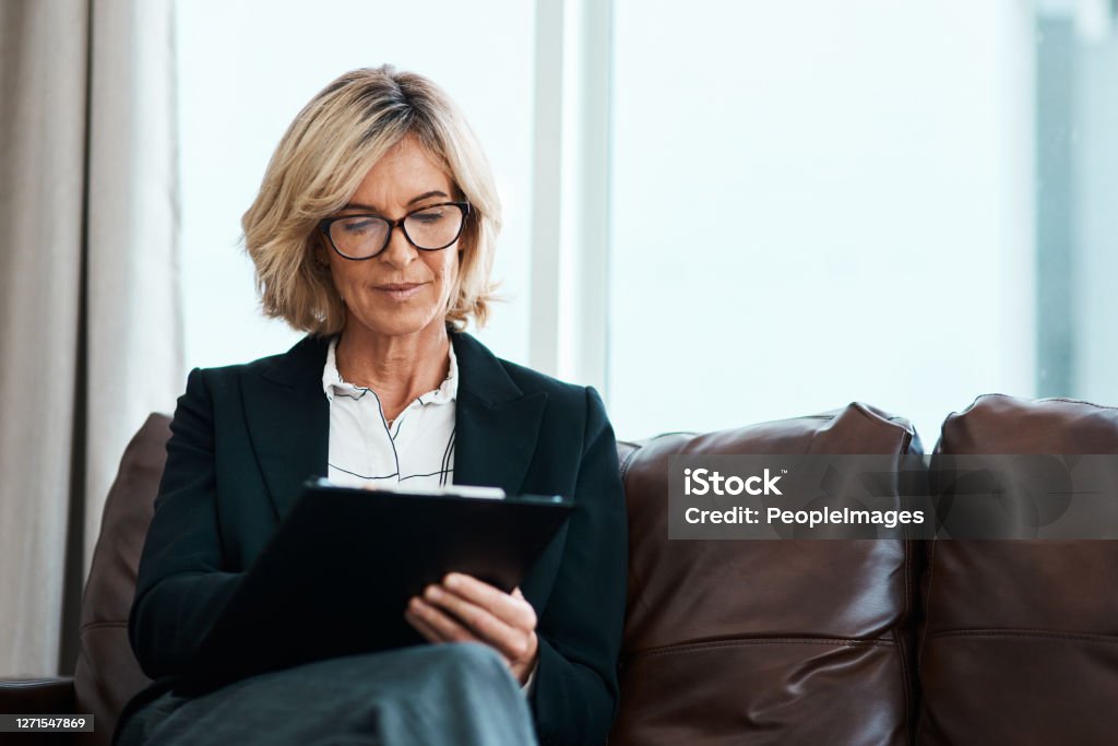 Feeling overwhelmed, your counsellor may be able to help Shot of a mature psychologist sitting on a sofa and writing notes on a clipboard Mental Health Professional Stock Photo