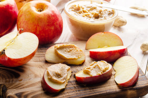 istock Cut board with apple slices with peanut butter on white wooden kitchen table 1271547900