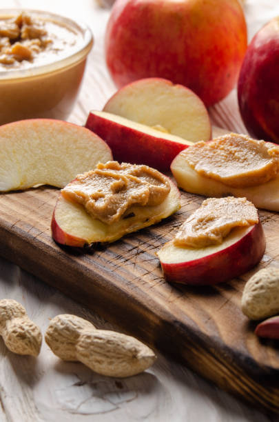 istock Cut board with apple slices with peanut butter on white wooden kitchen table 1271547902