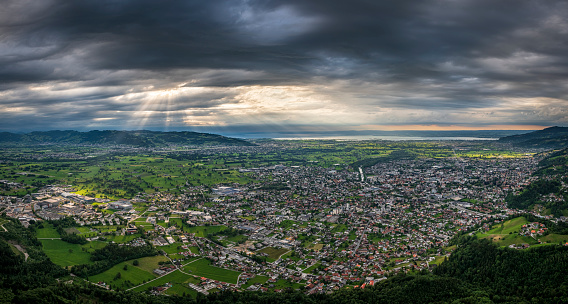 Aerial view of the town Dornbirn in Vorarlberg, the most western state of Austria. There is a dramatic sky with a few light beams between the clouds. In the background there is the lake of Constance.