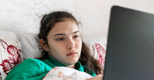 sad schoolgirl lies on sofa with laptop studying online sad schoolgirl in turquoise shirt lies on sofa with black laptop studying online staying home close view sad 15 years old girl stock pictures, royalty-free photos & images