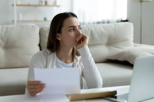 Thoughtful unhappy frustrated young woman holding paper letter with banking termination notification or eviction notice, thinking of financial problems bankruptcy or unexpected bad news alone at home.