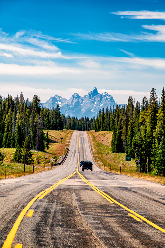 A mountain highway through the forest toward Grand Teton National Park, Wyoming with the peaks of the Tetons in the background.