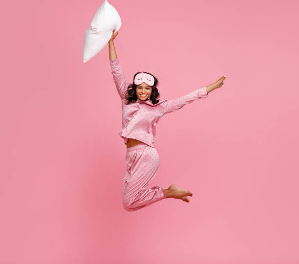 istock Excited woman in pajama jumping with pillow 1271553663