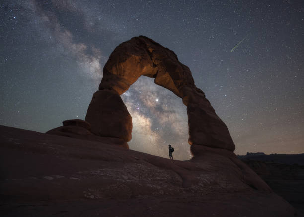 Silhouette of a hiker under Delicate Arch in Arches National Park at night Milky Way Galaxy and a shooting star with Delicate Arch in Arches National Park Utah delicate arch stock pictures, royalty-free photos & images