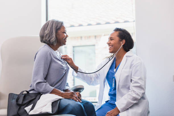 Cheerful doctor listens to patient's heartbeat A smiling female doctor listens to a senior female patient's heart during a medical exam. The patient smiles back at the doctor. listening to heartbeat stock pictures, royalty-free photos & images