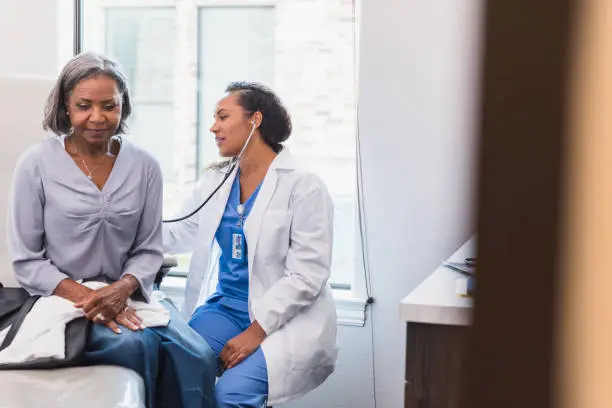 A mid adult female doctor uses a stethoscope to listen to a senior female patient's lungs during a medical exam.