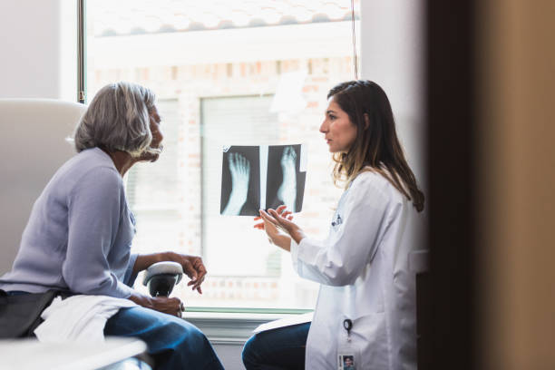 Caring doctor discusses patient's foot x-ray A serious female orthopedic doctor shows a senior female patient an x-ray of the patient's fractured foot. bone fracture stock pictures, royalty-free photos & images