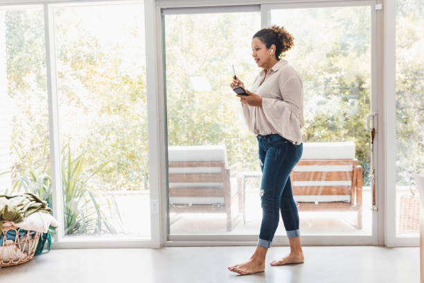 Woman walks as she chats with co-worker on phone The mid adult woman walks around her living room barefoot as she chats on her smart phone with a co-worker. walking into glass door stock pictures, royalty-free photos & images