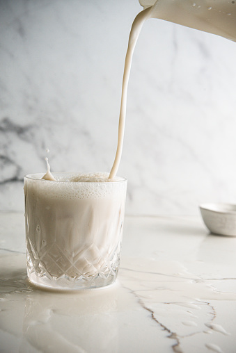 Pouring milk in a glass on a white marble top