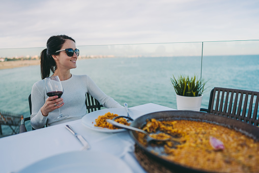 Woman in restaurant eating traditional spanish paella with glass of red wine