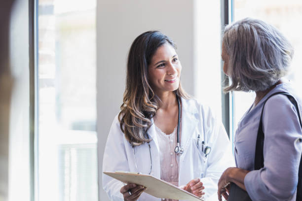 Doctor shares good news with senior patient A smiling doctor talks with a senior woman about good test results. The doctor is showing the results to the patient. female doctor stock pictures, royalty-free photos & images