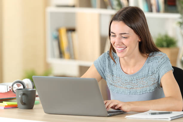 estudante feliz rindo usando laptop em uma mesa em casa - registo no computador - fotografias e filmes do acervo