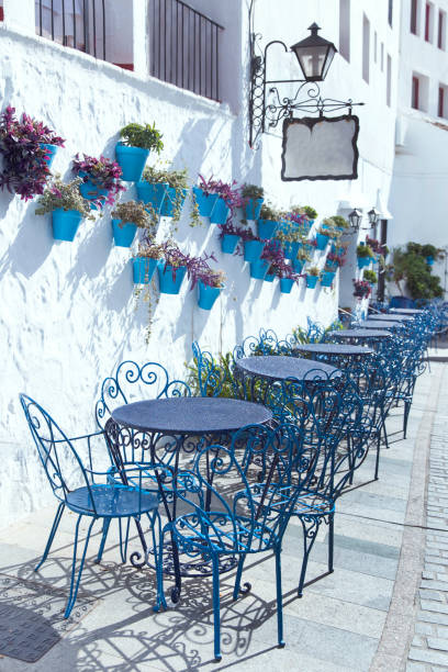 Mijas street. Charming white village in Andalusia, Costa del Sol Mijas street. Charming white village in Andalusia, Costa del Sol. Old blue metallic chair and table and beautiful flowers hanging on the white wall. mijas pueblo stock pictures, royalty-free photos & images