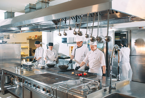 Five chefs wearing uniforms posing in a kitchen