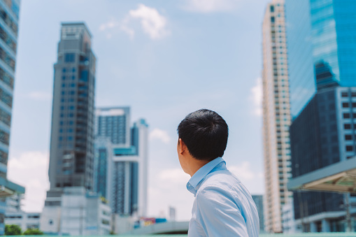 Businessman looking across towards city with tall modern buildings, head and shoulders of mid adult man, business, achievement, goals