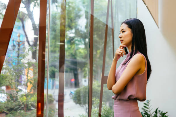 imprenditrice asiatica premurosa che guarda fuori dalla finestra nell'ufficio moderno - looking through window window business women foto e immagini stock