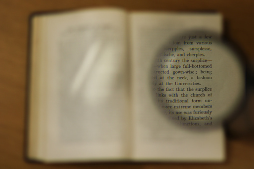 Part of a book page magnified with the use of a magnifying glass the whole book is blurred in the background with a magnified round section in focus