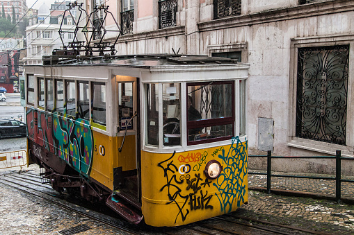 Traditional yellow tram covered with graffiti in a narrow street in Lisbon on a rainy Winter day.