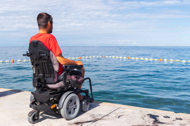 hombre sentado en silla de ruedas en la playa - cuadriplégico fotografías e imágenes de stock