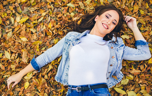 Young, beautiful, woman laying down on autumn leaves, in the public park, in autumn time. Day.